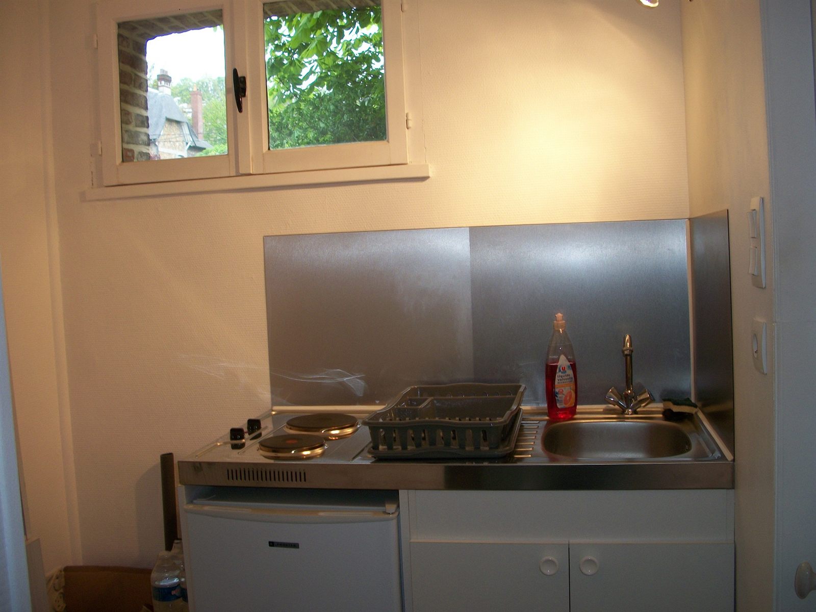 La cuisine séparée : évier, plaque deux feux, réfrigérateur et fenêtre sur les toits.